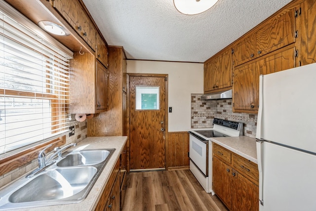 kitchen featuring brown cabinets, a sink, a textured ceiling, dark wood-style floors, and white appliances