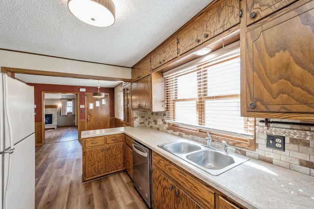 kitchen featuring a fireplace with raised hearth, a sink, freestanding refrigerator, brown cabinetry, and dishwasher