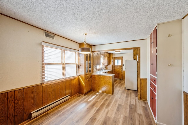 kitchen with a textured ceiling, freestanding refrigerator, wooden walls, wainscoting, and baseboard heating