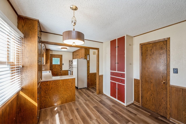 kitchen featuring a wainscoted wall, brown cabinets, freestanding refrigerator, and wood walls