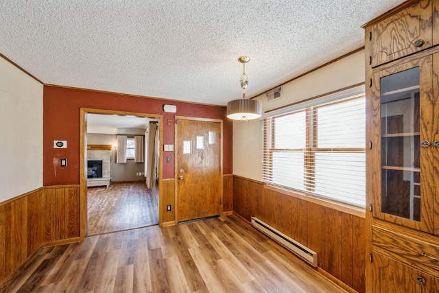 unfurnished dining area with a baseboard heating unit, wooden walls, a wainscoted wall, and a textured ceiling