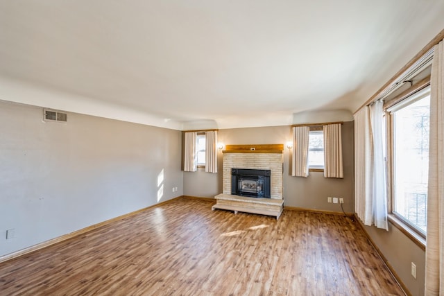 unfurnished living room with visible vents, a brick fireplace, baseboards, and wood finished floors