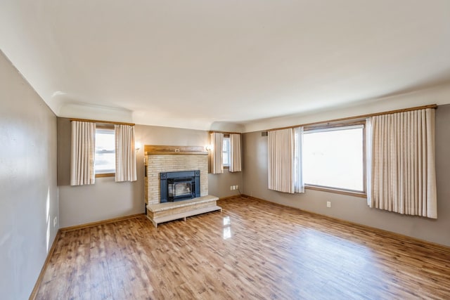 unfurnished living room featuring a fireplace, wood finished floors, baseboards, and a healthy amount of sunlight