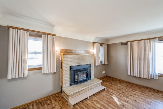 living room featuring a fireplace, wood finished floors, visible vents, and baseboards