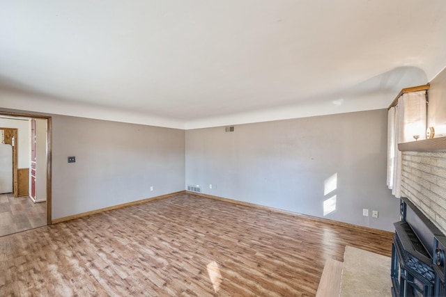 unfurnished living room with a brick fireplace, baseboards, visible vents, and light wood finished floors