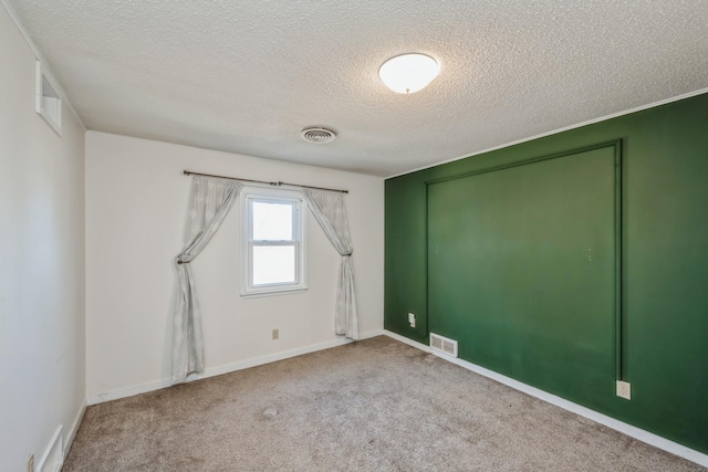 carpeted empty room featuring visible vents, a textured ceiling, and baseboards