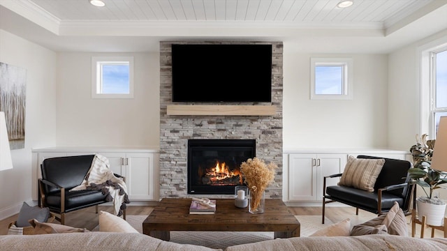 living area with light wood-style flooring, a fireplace, a raised ceiling, and ornamental molding