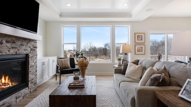 living area featuring a tray ceiling, plenty of natural light, light wood-style flooring, and a fireplace