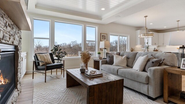 living room with plenty of natural light, a fireplace, a tray ceiling, and light wood-style floors