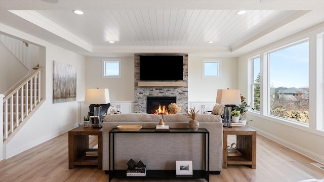 living room featuring a wealth of natural light, a tray ceiling, a fireplace, and light wood finished floors