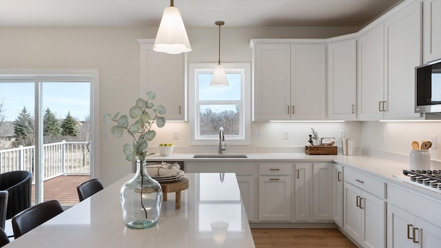 kitchen with a sink, decorative light fixtures, white cabinetry, light wood finished floors, and light countertops