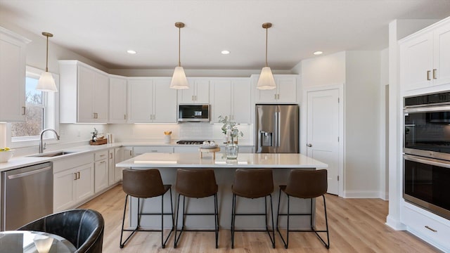 kitchen with a breakfast bar area, a kitchen island, a sink, stainless steel appliances, and white cabinetry