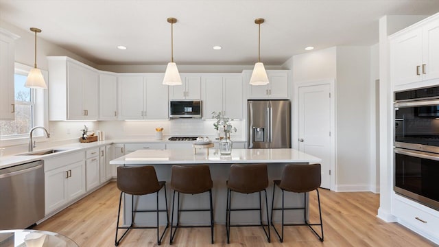 kitchen with a kitchen bar, a sink, a center island, stainless steel appliances, and white cabinets