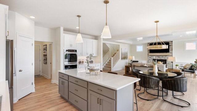 kitchen featuring gray cabinets, a stone fireplace, appliances with stainless steel finishes, open floor plan, and a center island