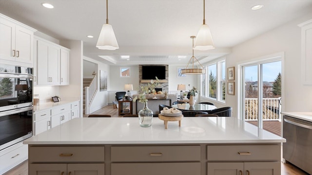 kitchen with light wood finished floors, gray cabinets, stainless steel appliances, a stone fireplace, and light countertops