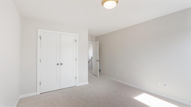 unfurnished bedroom featuring a closet, light carpet, and baseboards