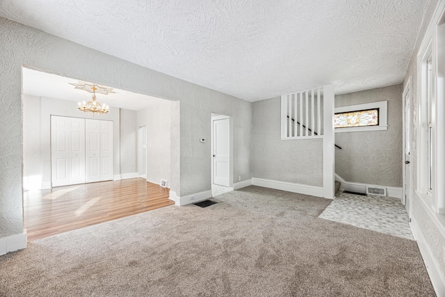 unfurnished living room featuring stairs, carpet flooring, a textured wall, and visible vents