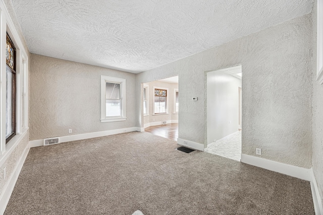 empty room featuring carpet floors, a textured ceiling, visible vents, and a textured wall