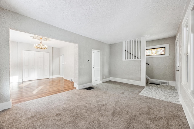 unfurnished living room with visible vents, stairs, carpet, and a textured wall