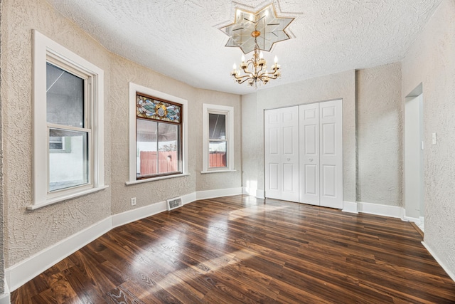 unfurnished bedroom featuring visible vents, baseboards, a textured wall, an inviting chandelier, and wood finished floors