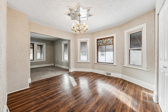 empty room featuring a chandelier, baseboards, wood finished floors, and a textured wall