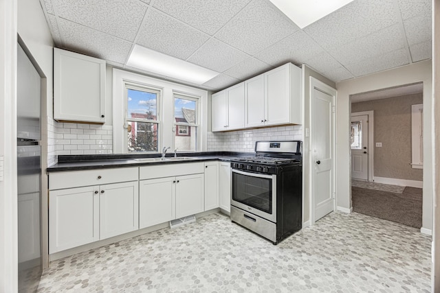 kitchen with baseboards, stainless steel gas range, a sink, white cabinetry, and dark countertops