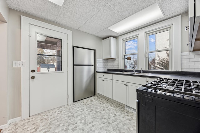 kitchen with a sink, dark countertops, freestanding refrigerator, gas stove, and light floors