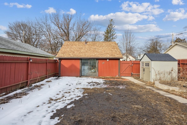 snowy yard featuring an outdoor structure, a fenced backyard, a storage shed, and a gate