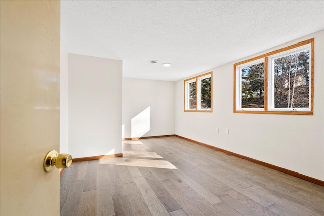 empty room with baseboards, a textured ceiling, and wood finished floors