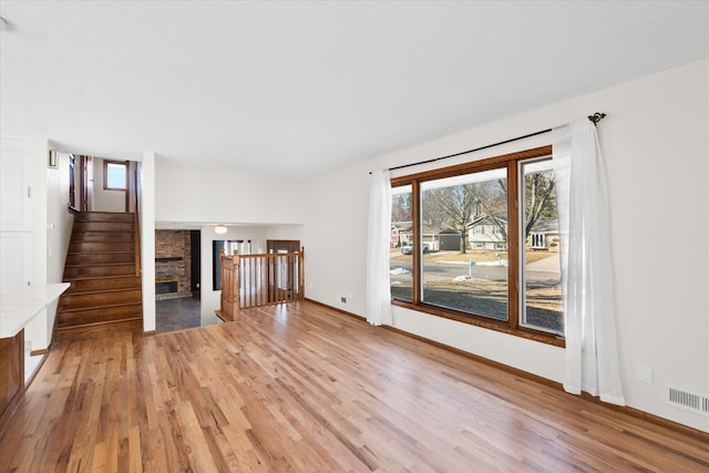 unfurnished living room featuring stairs, light wood-style flooring, a fireplace, and visible vents