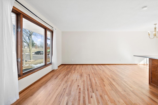 unfurnished living room featuring baseboards, light wood-style floors, and an inviting chandelier