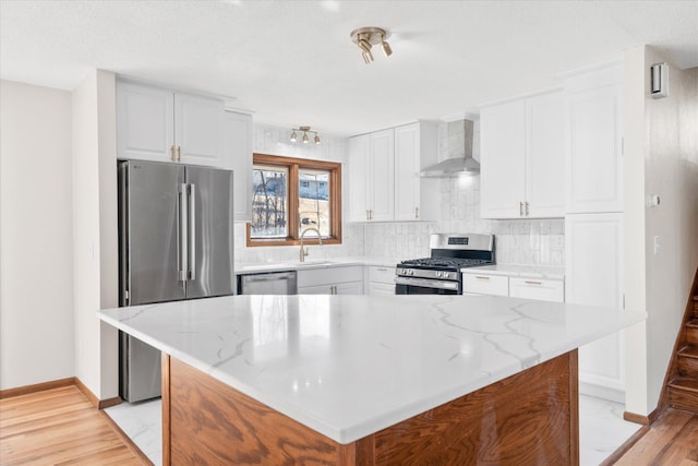 kitchen featuring backsplash, light stone counters, appliances with stainless steel finishes, white cabinetry, and wall chimney exhaust hood