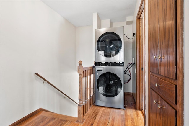 washroom featuring stacked washer / drying machine, baseboards, and light wood-style flooring