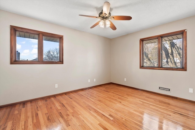 spare room featuring a wealth of natural light, ceiling fan, light wood finished floors, and baseboards