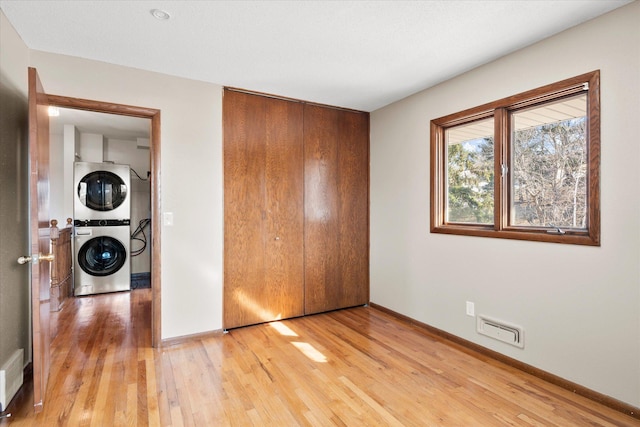 unfurnished bedroom featuring a closet, visible vents, stacked washer / drying machine, and light wood finished floors