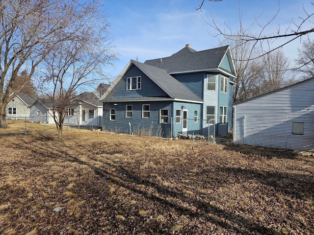 rear view of property with a chimney, roof with shingles, and fence