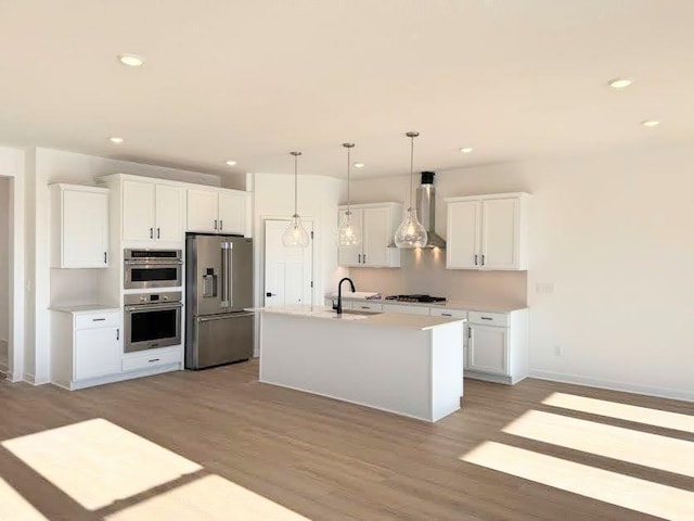 kitchen with a sink, stainless steel appliances, white cabinets, light wood-style floors, and wall chimney range hood