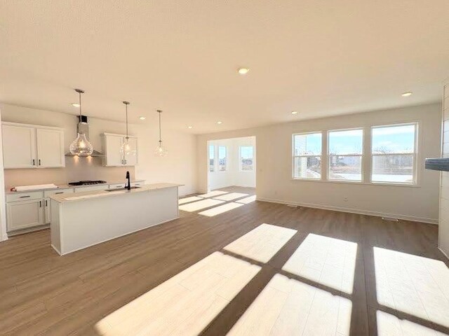 kitchen with a healthy amount of sunlight, dark wood finished floors, gas stovetop, a sink, and wall chimney exhaust hood