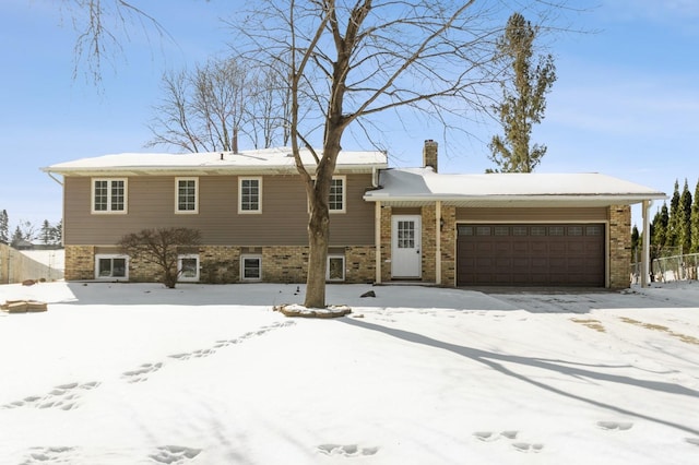 split level home featuring brick siding, a chimney, a garage, and fence