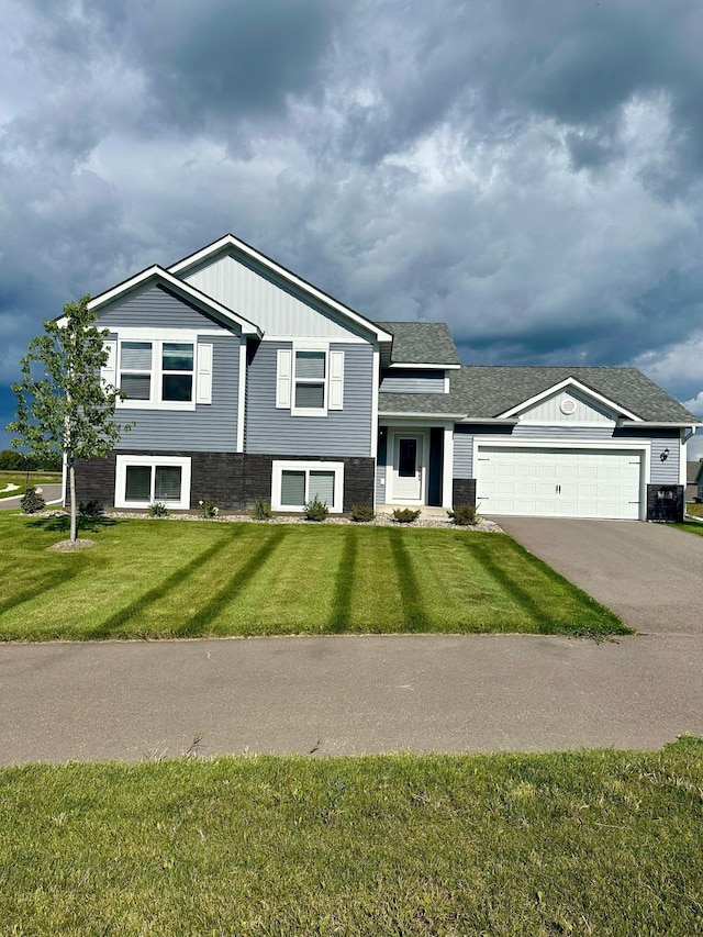 split level home featuring an attached garage, a shingled roof, driveway, and a front yard