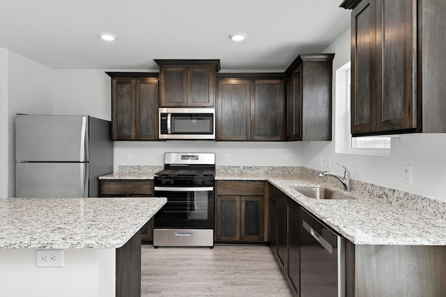 kitchen featuring recessed lighting, a sink, stainless steel appliances, dark brown cabinetry, and light wood-style floors