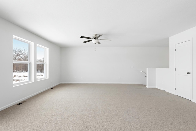 spare room with a ceiling fan, light colored carpet, visible vents, and baseboards