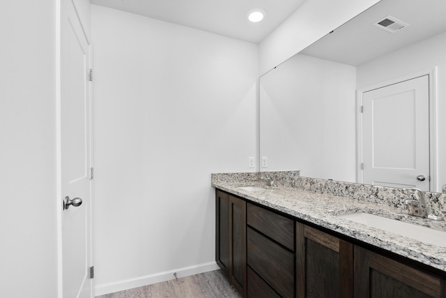 bathroom featuring visible vents, baseboards, double vanity, wood finished floors, and a sink