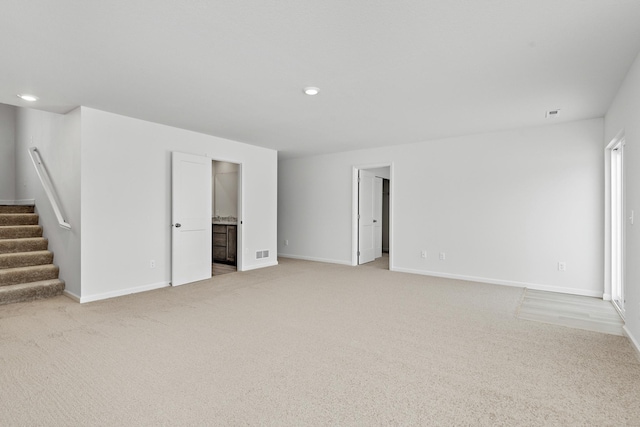 spare room with stairway, light carpet, baseboards, and visible vents