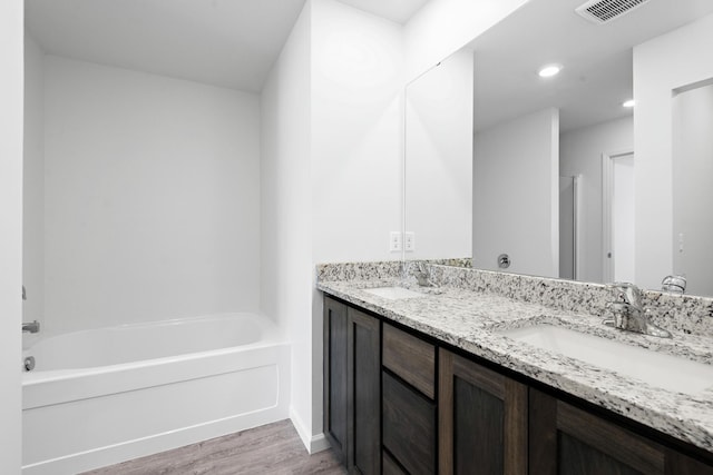 bathroom with a bath, visible vents, wood finished floors, and a sink