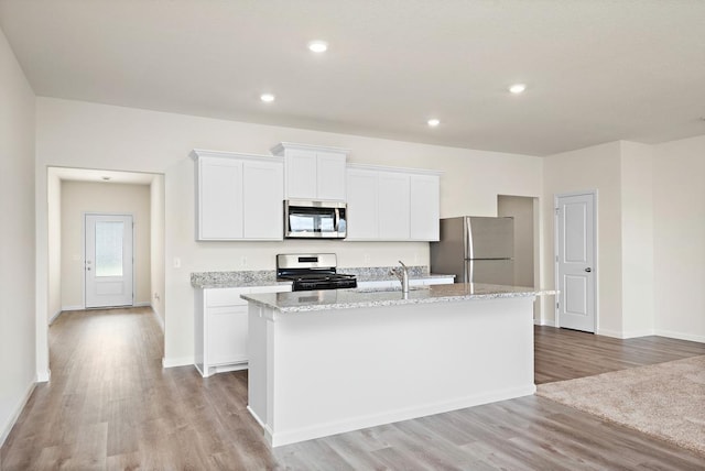 kitchen featuring light wood finished floors, a kitchen island with sink, white cabinets, stainless steel appliances, and a sink