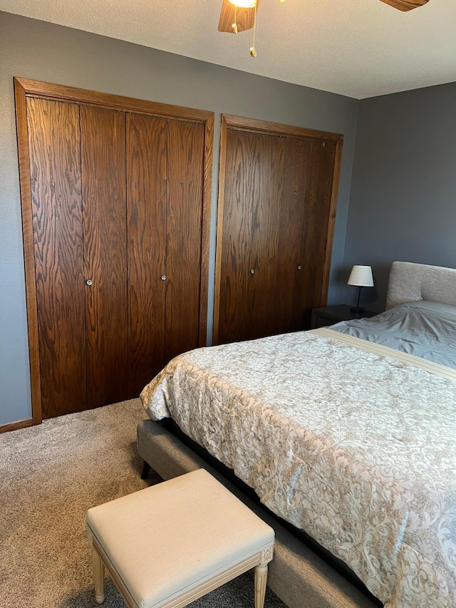 carpeted bedroom with two closets, ceiling fan, and a textured ceiling