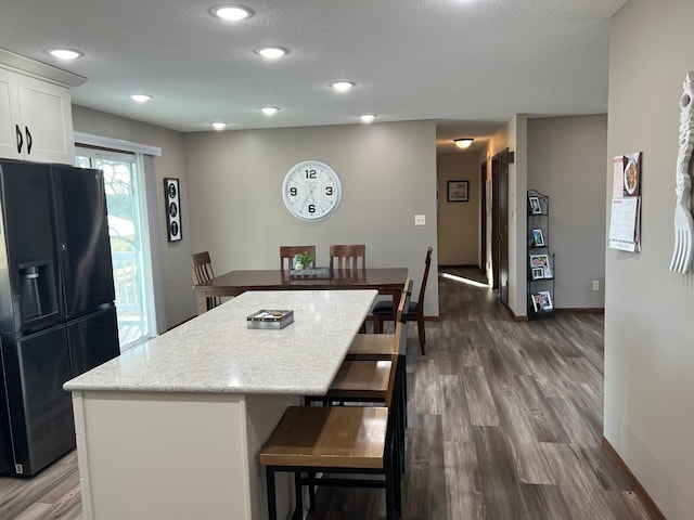 kitchen featuring black fridge, dark wood finished floors, a center island, white cabinetry, and baseboards