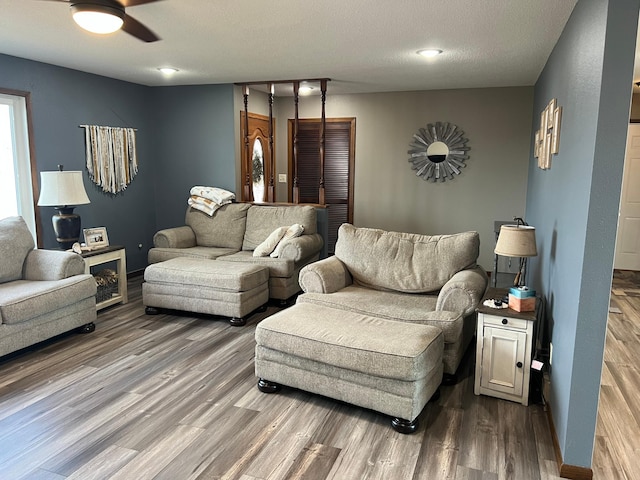 living room featuring a textured ceiling, a ceiling fan, baseboards, and wood finished floors