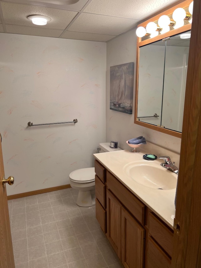 bathroom with a drop ceiling, toilet, vanity, and baseboards